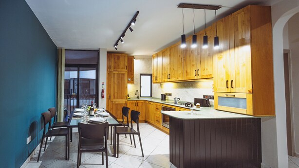 A modern kitchen with wooden cabinets, a dining area with chairs, and a large island. - Three bedroom Apartment (Il-Gżira)