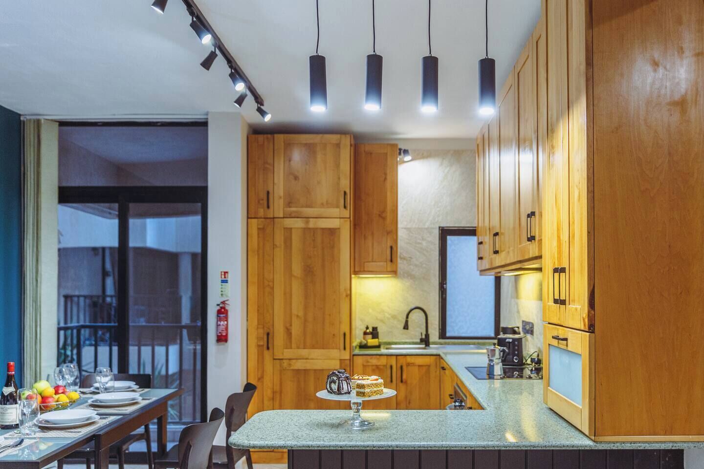 A modern kitchen with wooden cabinets, a granite countertop, and pendant lighting.