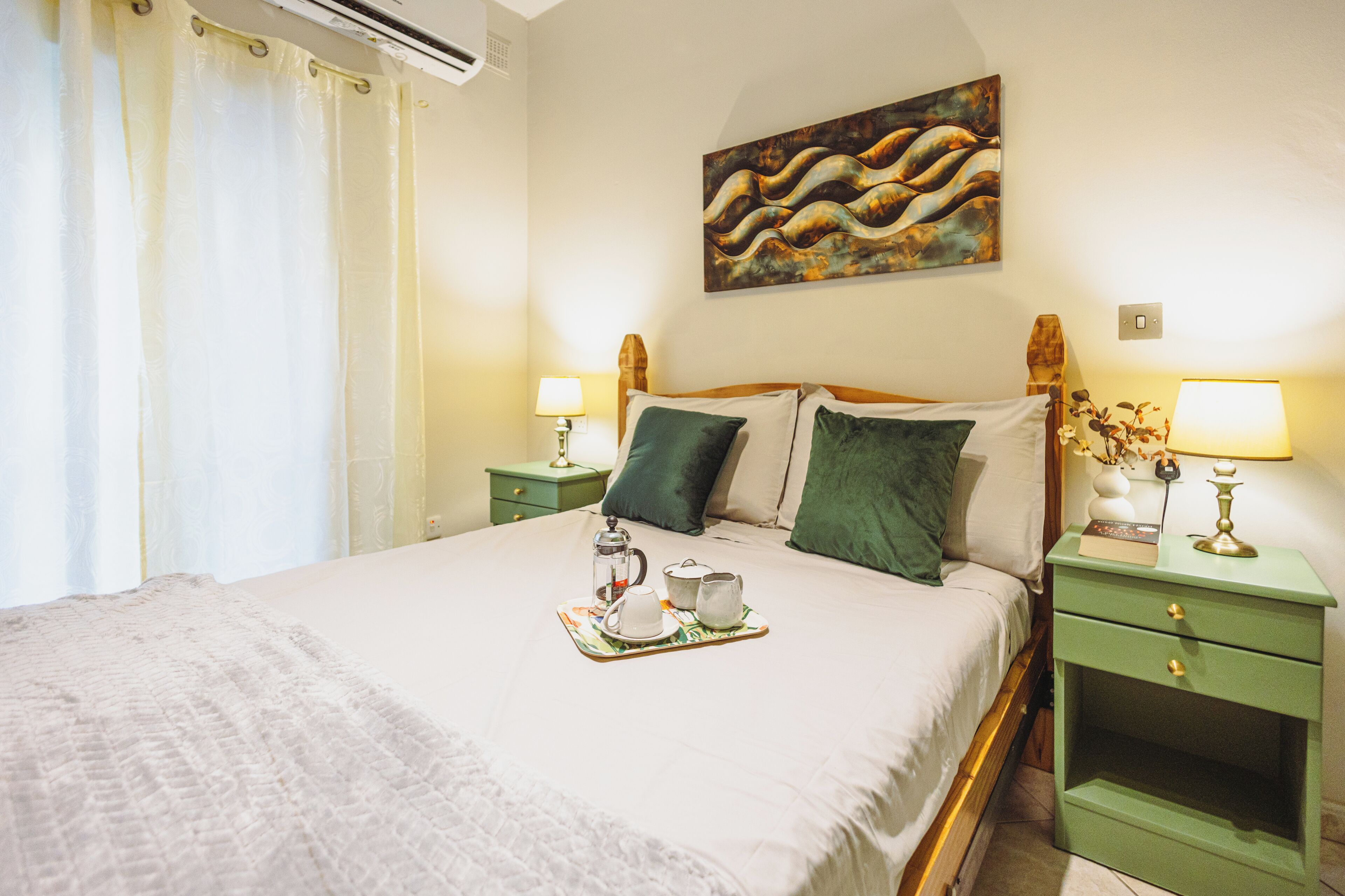 Cama bem arrumada com uma bandeja de chá, duas luminárias de cabeceira e um quadro na parede.