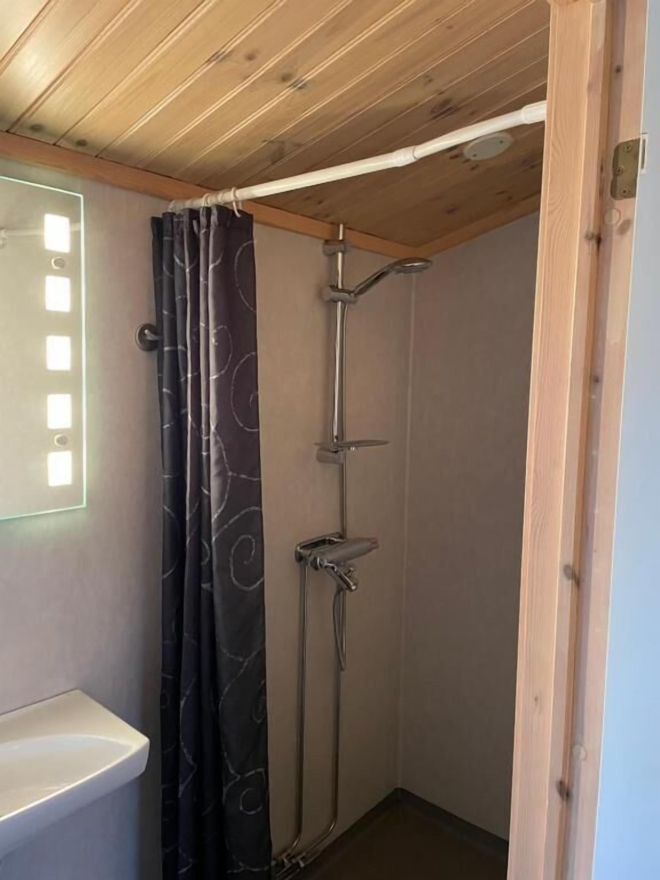 A shower with a curtain, a wooden ceiling, and a white sink.