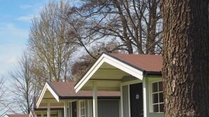 A row of single-story cabins with front porches, each with a small set of steps leading to the entrance. - Skara Stadscamping & Stugby (Skara)