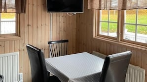 A wooden-paneled room with a table and chairs, a flat-screen TV mounted on the wall, and windows with curtains. - Skara Stadscamping & Stugby (Skara)