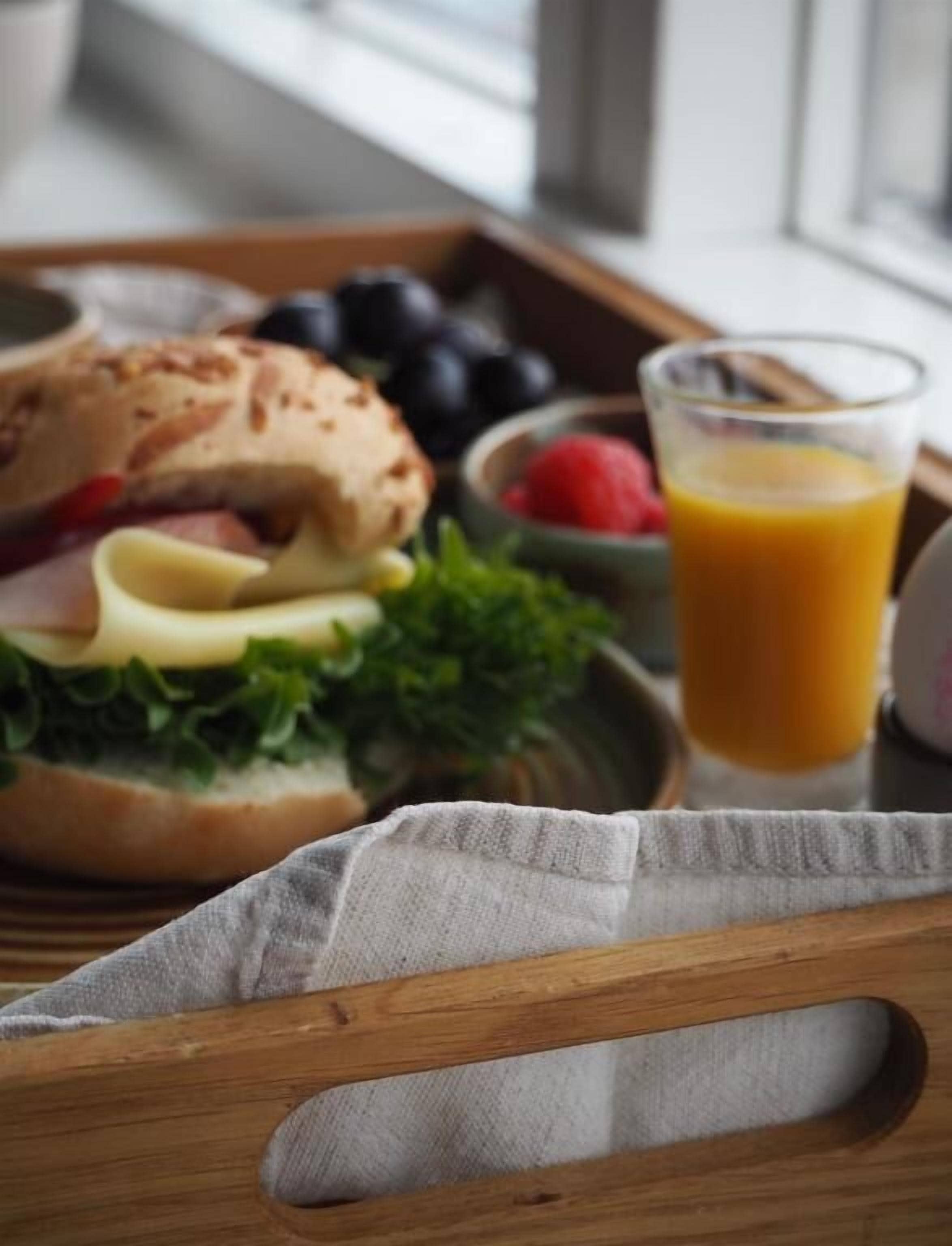 Bandeja de desayuno con un sándwich, frutos rojos y un vaso de jugo de naranja.
