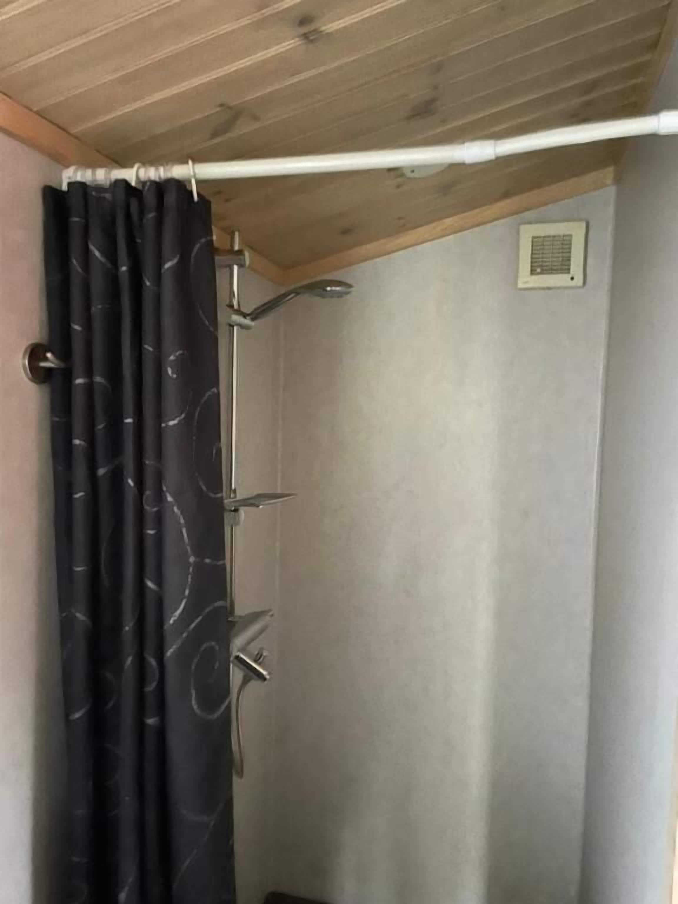Une douche avec un rideau noir, un pommeau de douche à main et un panneau de commande fixé au mur.