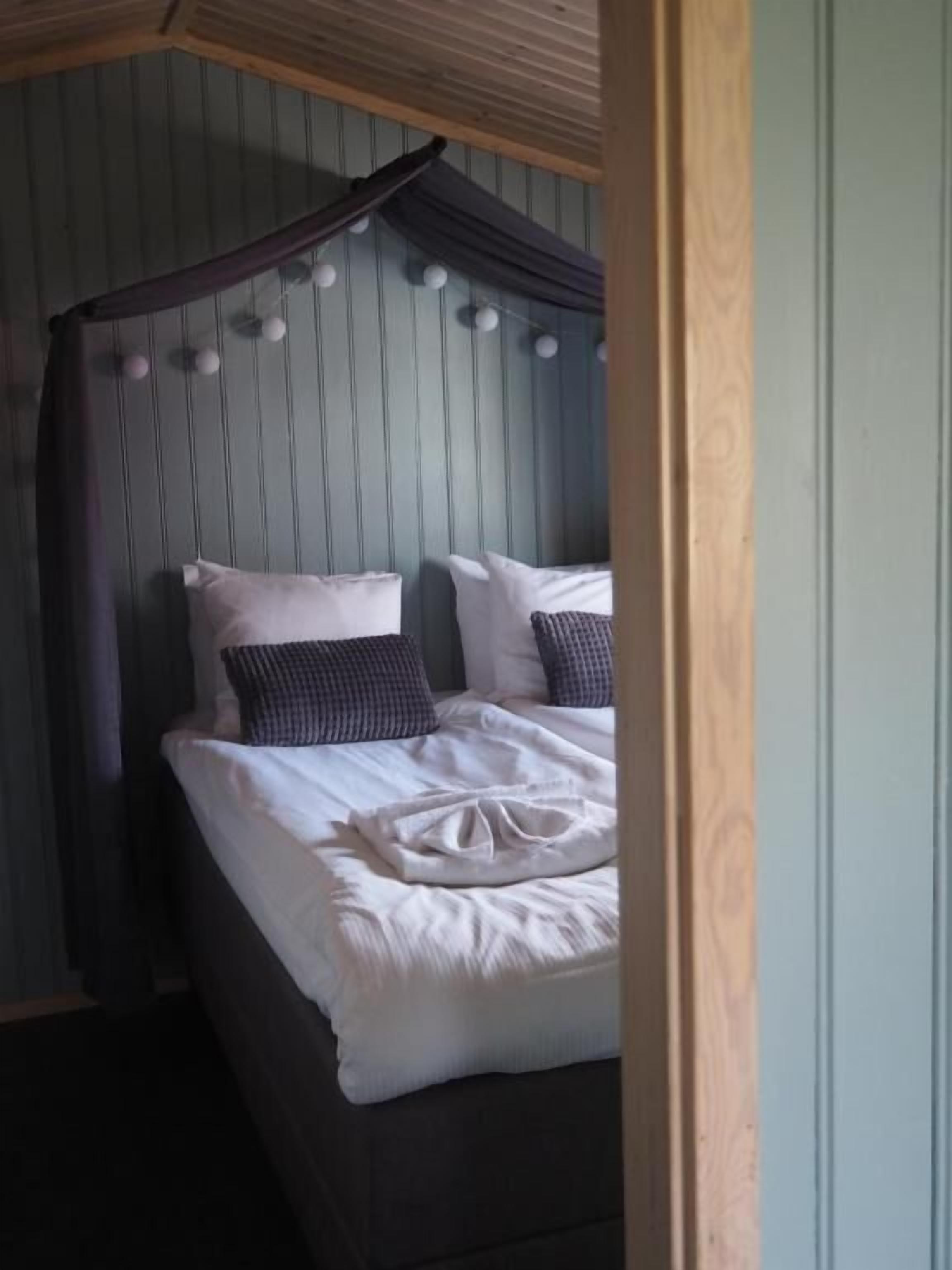 Una cama con ropa de cama blanca y dosel, cabecero de madera y pared con paneles verticales.