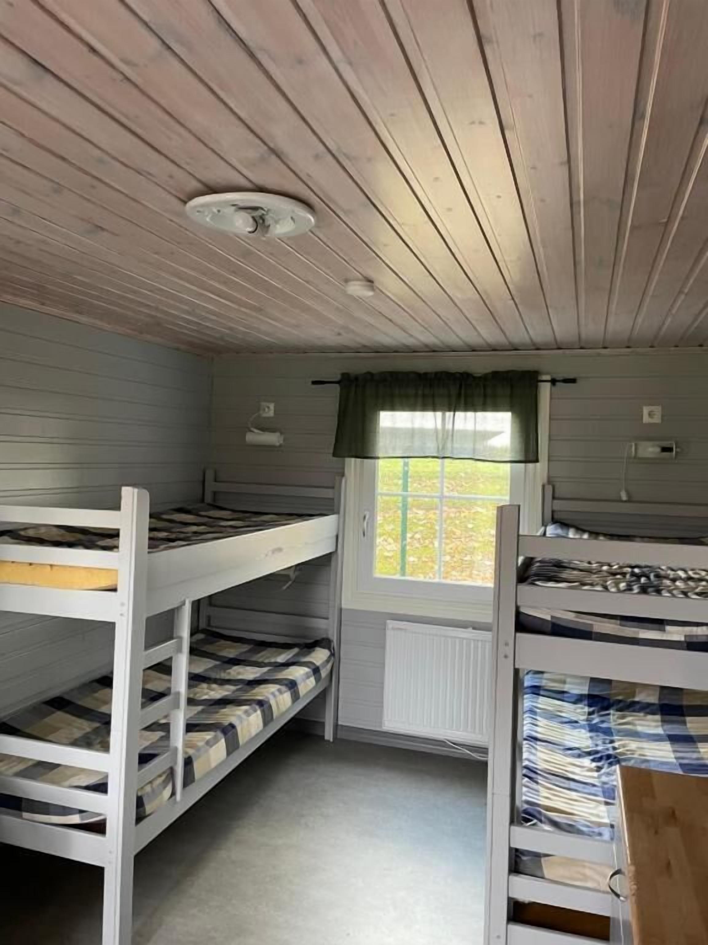Une pièce avec des lits superposés, une fenêtre avec un rideau et un luminaire au plafond.