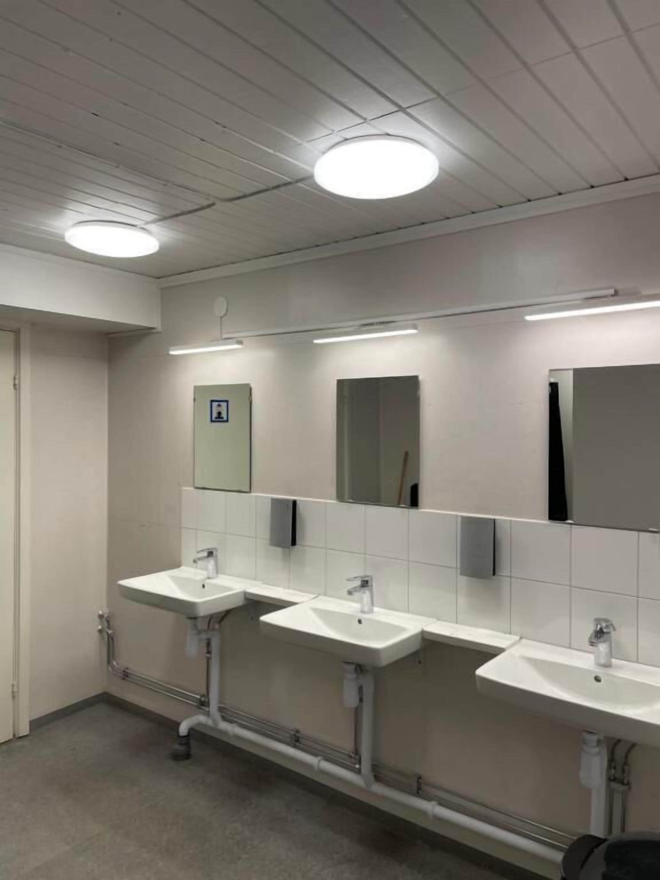 A restroom with three sinks, a mirror, and overhead lighting.