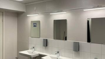 A restroom with three sinks, a mirror, and overhead lighting.