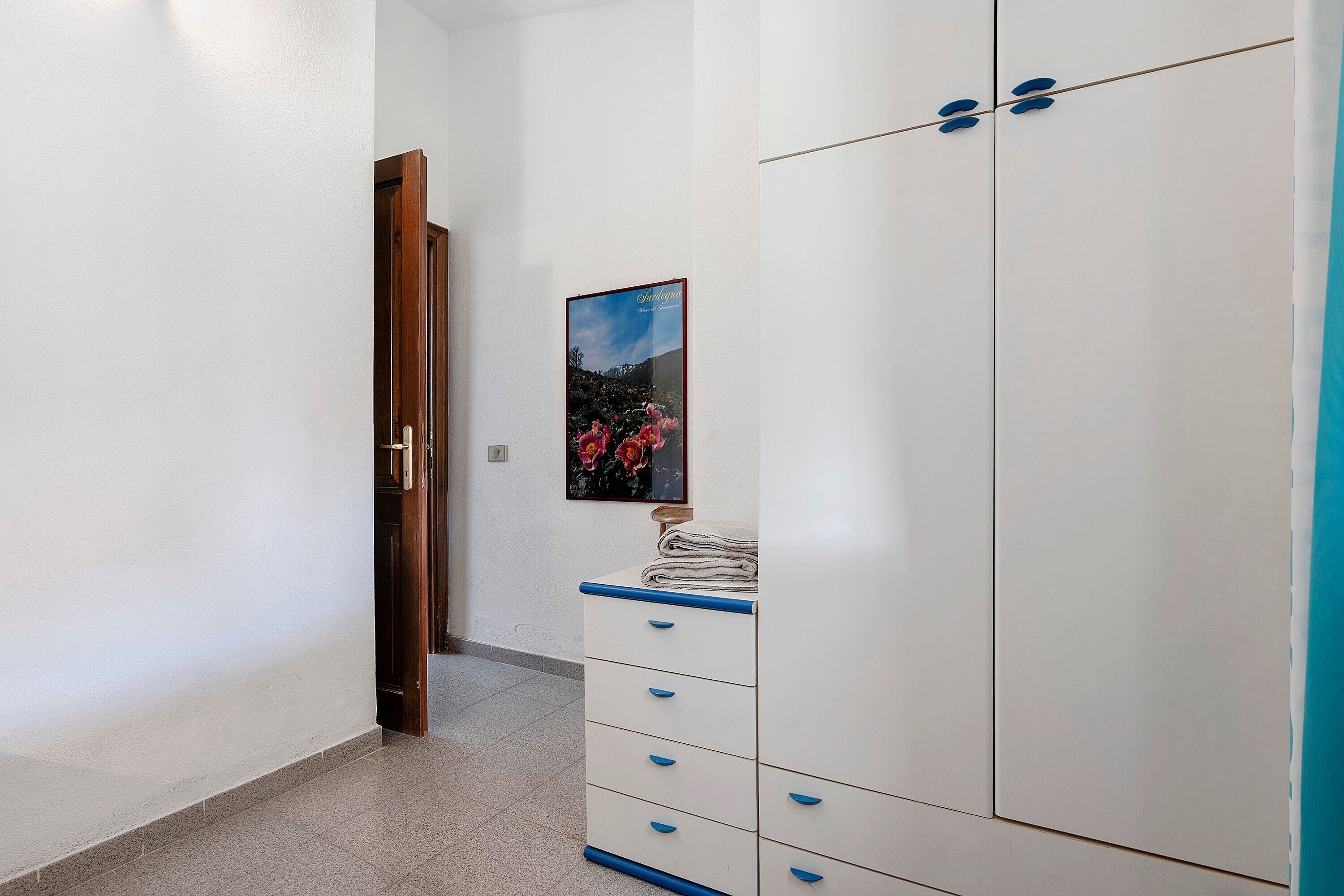 A hallway with a white wardrobe, a wooden door, and a framed picture on the wall.