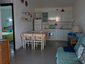 A compact living space with a dining table, chairs, a sofa, a kitchenette, and a bed.