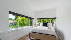 Ein modernes Schlafzimmer mit einem Bett, zwei Fenstern und Blick auf Grünflächen.