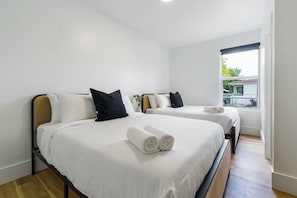 Habitación de hotel con dos camas, ropa de cama blanca, almohadas negras y una ventana con vistas al exterior.