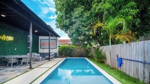 Ein rechteckiger Pool mit einer umlaufenden Terrassenfläche, einem Neonlichtschild und einer Wand mit dem Schriftzug 'NETFLIX'.