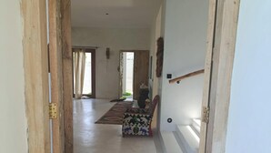 A hallway with a wooden door, a patterned bench, and a rug leading to a room with a window. - Stunning newly built villa located 50 meters from Fortamu Beach (Watamu)
