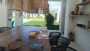 A dining area with a wooden table, chairs, and a view of a swimming pool and garden. - Stunning newly built villa located 50 meters from Fortamu Beach (Watamu)