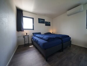 A bedroom with a bed, a bedside table, a lamp, a window with curtains, and two wall-mounted pictures. - Cube Magnifique 6 (Nijkerk)
