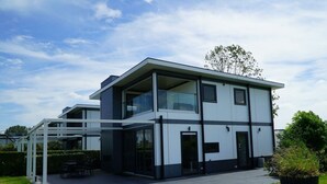 A modern two-story building with large windows, a covered outdoor seating area, and a well-maintained lawn. - Cube Magnifique 6 (Nijkerk)
