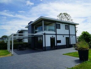 A modern two-story building with large windows, a covered outdoor seating area, and a well-maintained lawn. - Cube Magnifique 6 (Nijkerk)