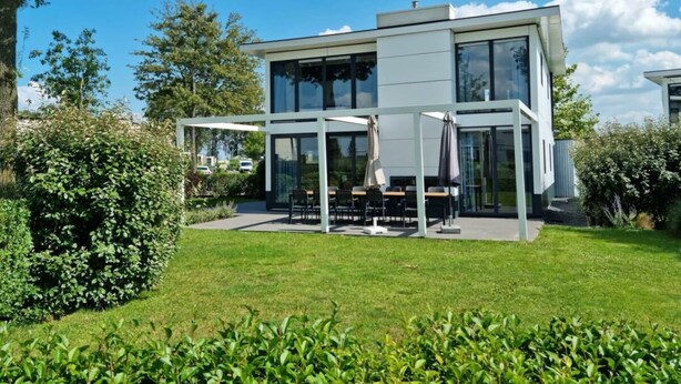 Ett modernt hus i två våningar med en uteplats, omgivet av grönska.