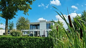 Ett modernt hus i två våningar med en glasfasad, omgivet av en välskött häck och högt gräs.