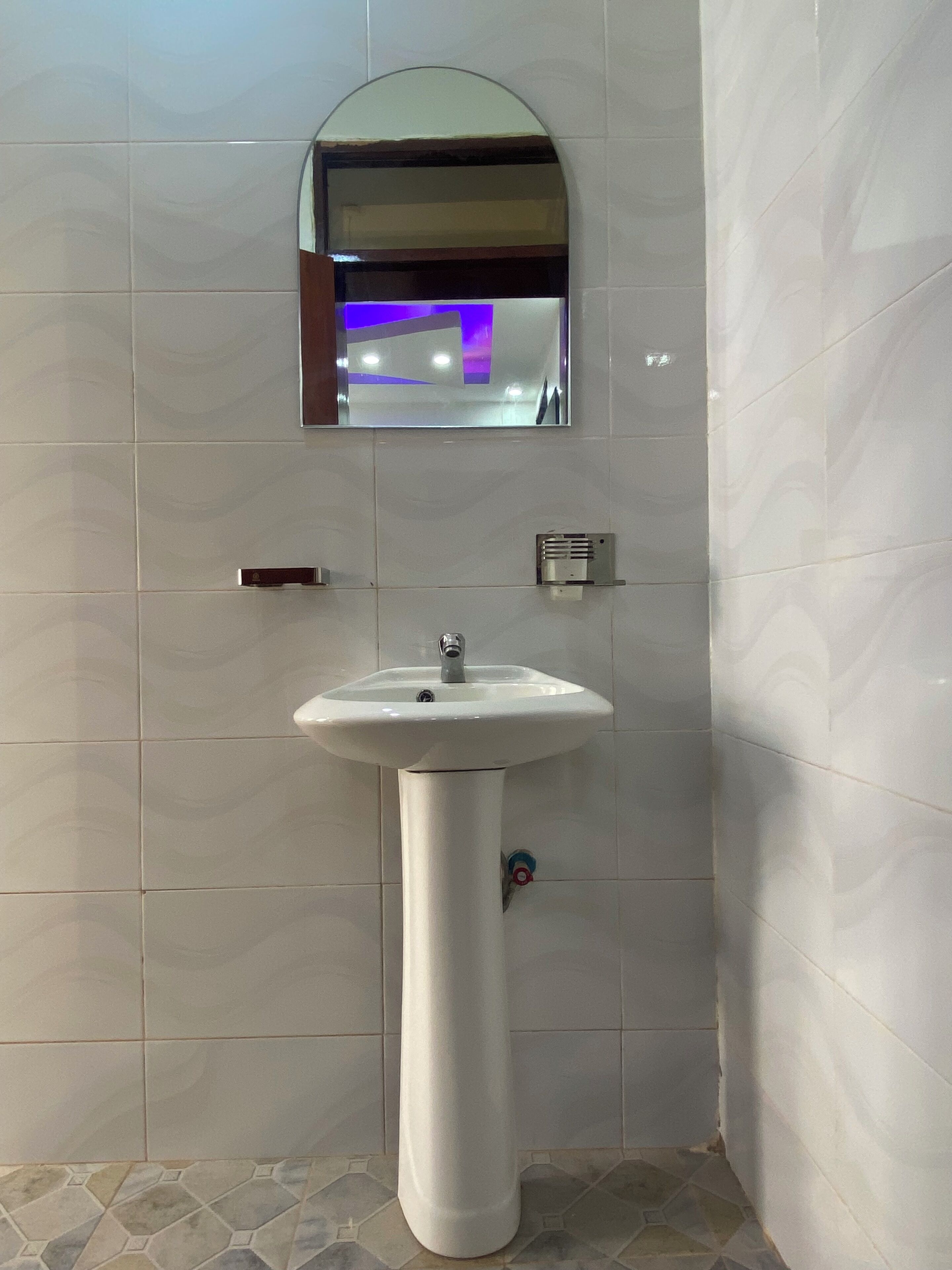 Een badkamer met een wastafel op een voetstuk, een spiegel en een ventilatie-unit aan de muur.