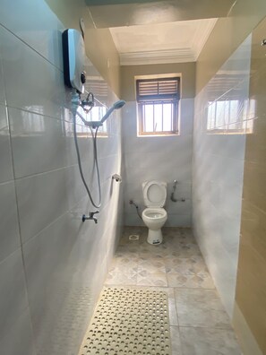 A small bathroom with a toilet, a shower, and a window. - Neriah Suites where comfort is guaranteed (Kabale)