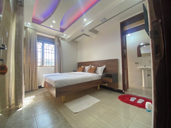 A modern bedroom with a wooden bed, a bedside table, a mirror, a window with curtains, and a red rug. - Neriah Suites where comfort is guaranteed (Kabale)