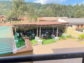 A covered outdoor seating area with tables and chairs, surrounded by greenery and a view of a hilly landscape. - Neriah Suites where comfort is guaranteed (Kabale)
