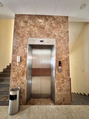 An elevator with a digital display, a trash bin, and a marble wall. - Klei Buon Ma Thuot City Centre (Buon Ma Thuot)