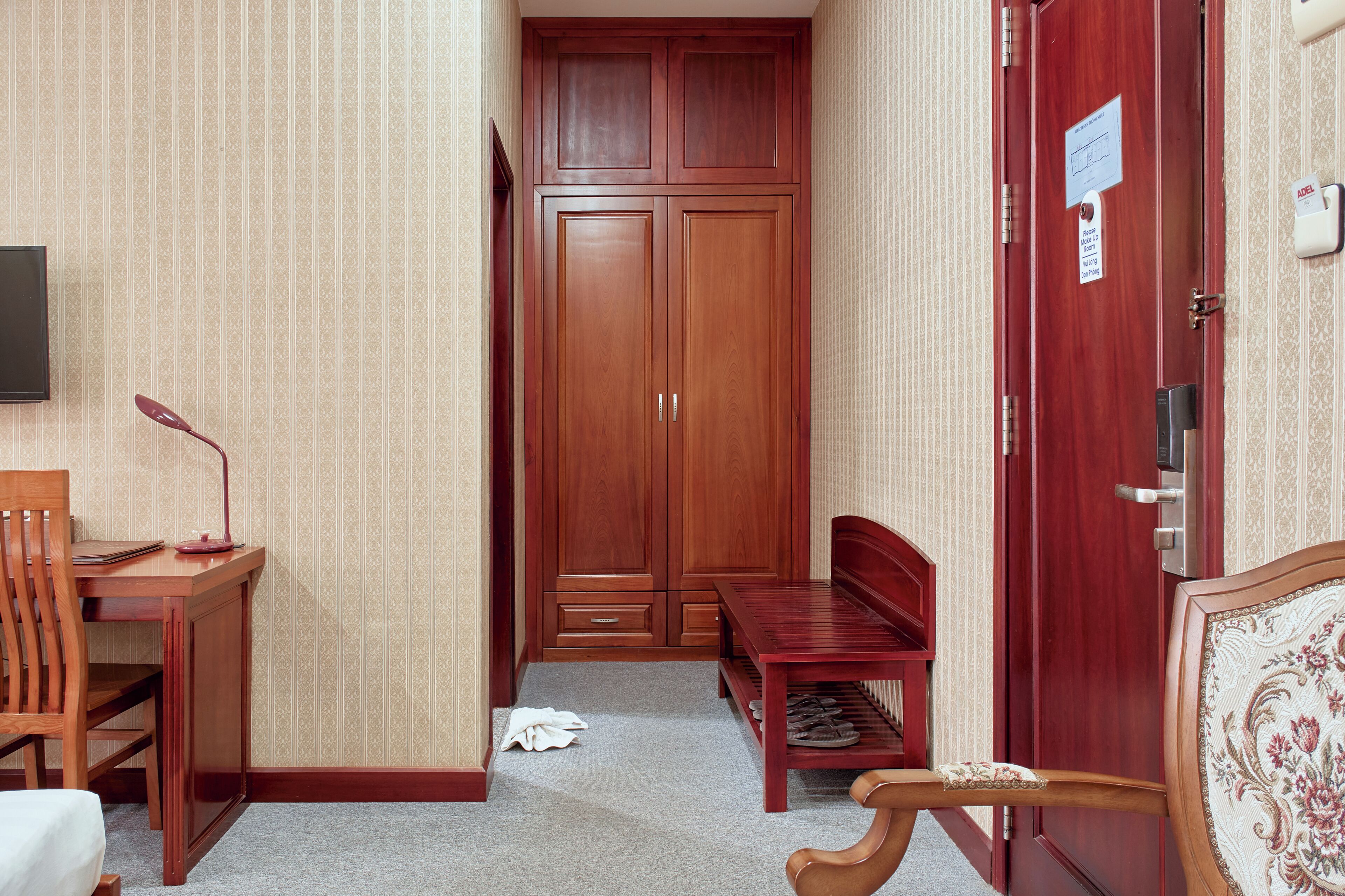 Habitació d'hotel amb un armari de fusta, un escriptori amb una cadira, una banca i una porta amb un rètol.
