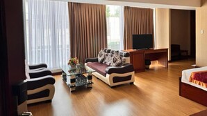 A hotel room with a sofa, a glass coffee table, a TV, and a bed.