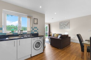 A modern kitchen with a washing machine, a dining area with a glass table, and a living room with a sofa. - Heathrow Living 2BDR 2BA Apt 02-360stays (Stanwell)