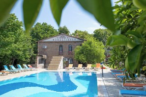 En swimmingpool med liggestole, en murstensbygning med teksten 'MANASTIRHAN', og frodig vegetation omkring.