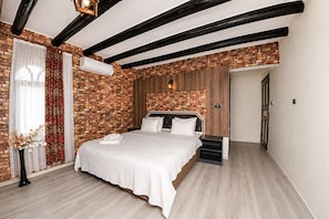 A bedroom with exposed wooden beams, a brick wall, a bed with white linens, and a small bedside table. - Antik Manastır İda  (Edremit)