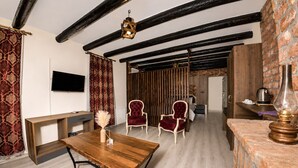 Una habitación con vigas de madera a la vista, una mesa de madera con sillas, un televisor y una lámpara.