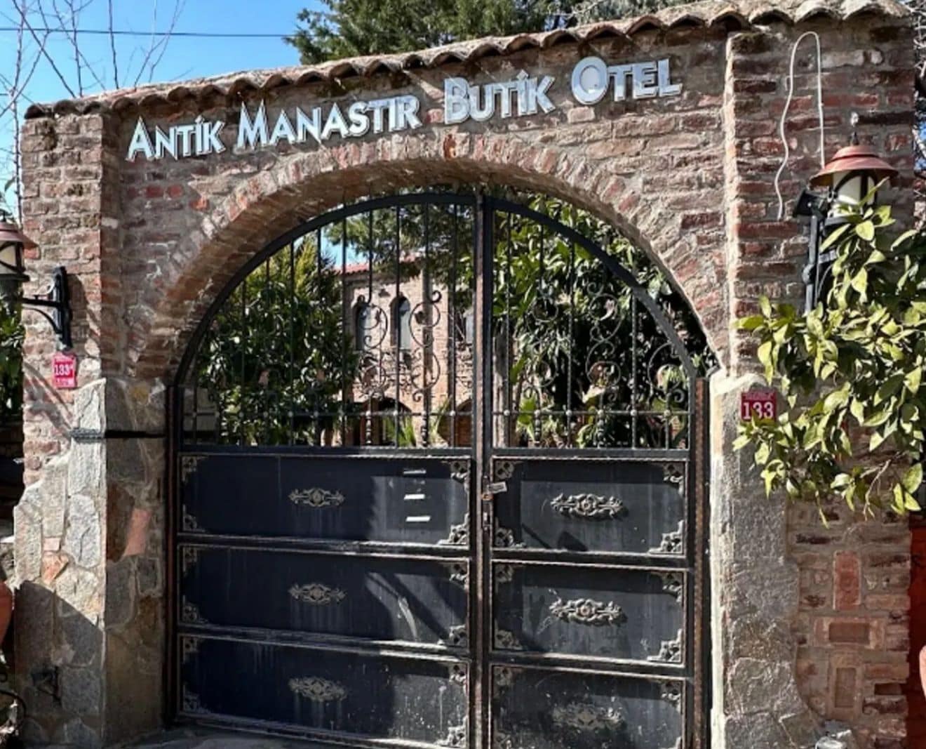 Un arco in mattoni con il cartello 'ANTIK MANASTIR BUTIK HOTEL' sopra un cancello nero.