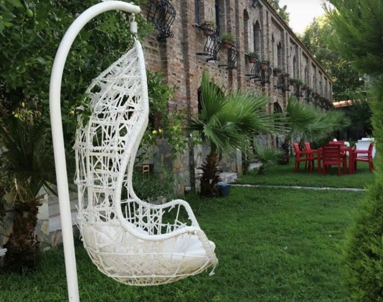 A white hanging chair in a garden with a brick building in the background.