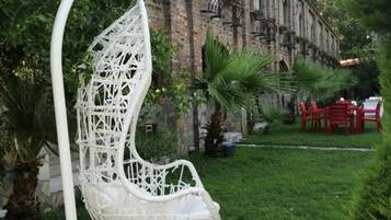 A white hanging chair in a garden with a brick building in the background.