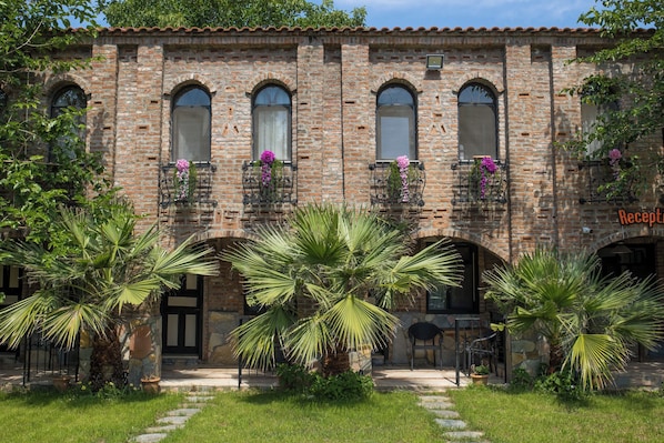 A brick building with arched windows and a garden with palm trees.