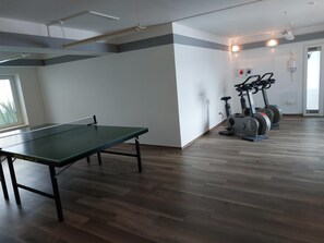 Ein Zimmer mit Tischtennisplatte, Ergometer und einem Fenster.