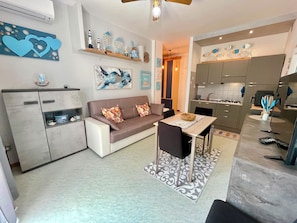 Eine moderne Küche mit grauen Schränken, einem Esstisch mit Stühlen, einer Couch mit floralen Kissen und einem Deckenventilator.