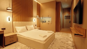 A modern bedroom with a large bed, bedside tables, a built-in TV, and a small kitchenette. - Europa  (Semey)