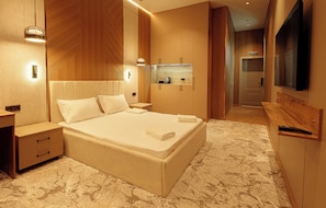 A modern bedroom with a large bed, bedside tables, a built-in TV, and a small kitchenette. - Europa  (Semey)