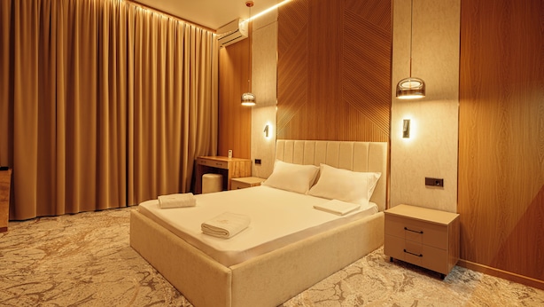 A hotel room with a large bed, bedside tables, a desk, and a large window with curtains. - Europa  (Semey)