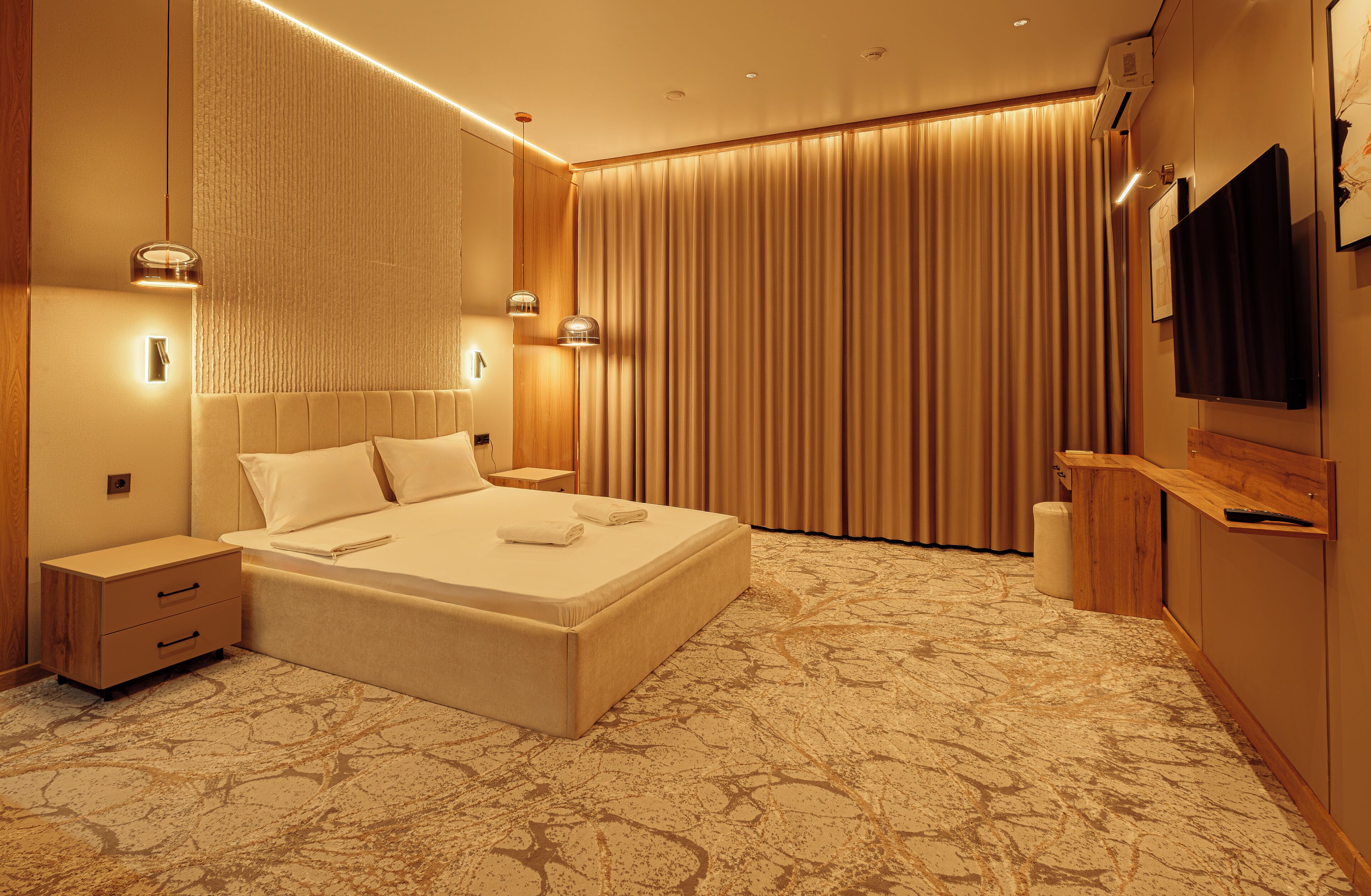 A modern hotel room with a large bed, bedside lamps, a flat-screen TV, and a wooden nightstand.
