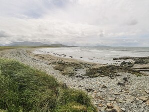 A coastal landscape with a pebble beach, grassy areas, and distant mountains under a cloudy sky. - ISLANDS INN, pet friendly, with a garden in Louisburgh, County Mayo (Louisburgh)