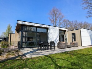 Ein modernes Haus mit großen Fenstern, einer Terrasse mit Gartenmöbeln und einem kleinen Garten.