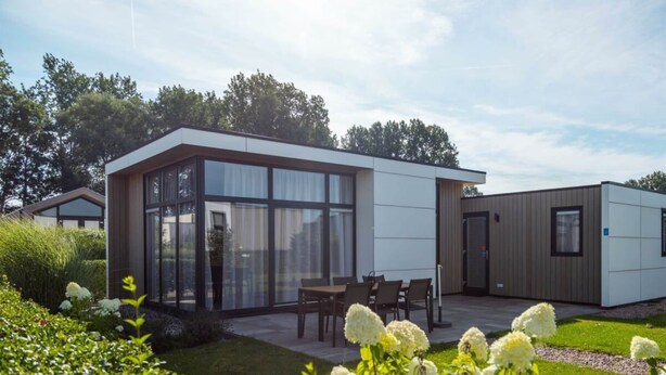 A modern building with large windows, a patio with chairs, and a garden with white flowers. - Holiday Home in Nijkerk With Terrace (Nijkerk)