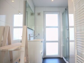Ein modernes Badezimmer mit einer Duschkabine aus Glas, einem weißen Waschbecken und einem großen Fenster.