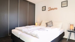 A modern bedroom with a large bed, dark sliding doors, and a wall-mounted lamp. - Holiday Home in Nijkerk With Terrace (Nijkerk)